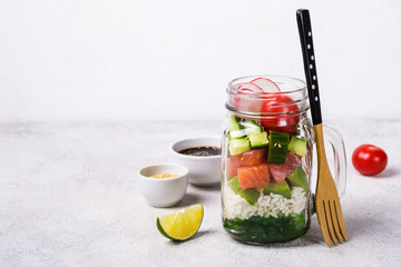 Hawaiian salmon poke salad in glass jar with rice and vegetables on gray background