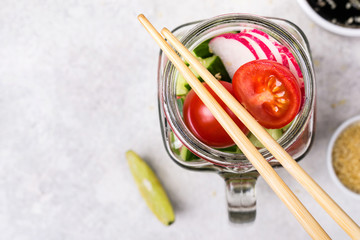 Fototapeta na wymiar Hawaiian salmon poke salad with vegetables in glass jar and chopsticks, selective focus