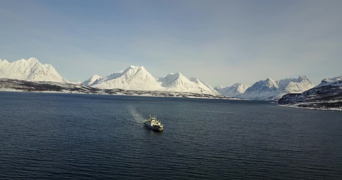 drone footage of a large cruise ship preparing to dock on port from cold water sea,with real life fantasy painted style of snow mountain,bare trees,blue sky and sunlight up above.norway in 4k 24fps