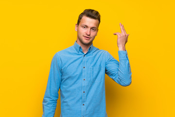 Blonde man over isolated yellow wall with problems making suicide gesture