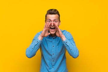 Blonde man over isolated yellow wall shouting and announcing something