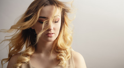 Naklejka premium soft studio portrait of a beautiful young woman, girl face with curly hair disheveled from wind , the concept of natural beauty, body care, cosmetics