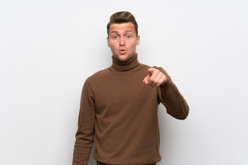 Blonde man over isolated white wall surprised and pointing front