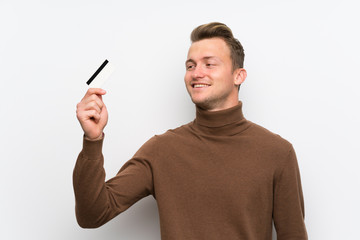 Blonde man over isolated white wall holding a credit card and thinking