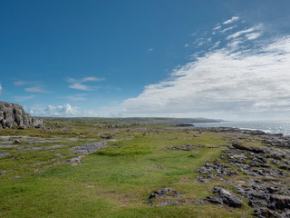 Sunny day in county Clare, Burren, Ireland, patches of green grass next to rock formations, Clouds over Atlantic ocean.