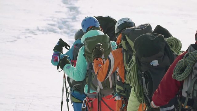 tourists follow each other along the trampled path. they have on their backs heavy backpacks and equipment and long cables.
