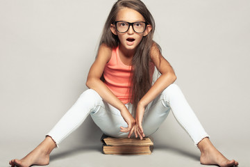 Portrait of a shocked funny girl sitting on manuels over light gray background in summer season...