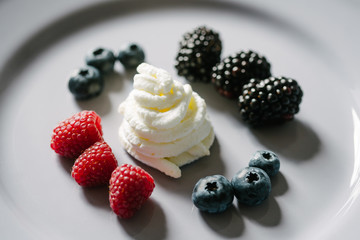 Close up view on a delicious, decorative dessert made from berry mix (raspberries, blueberries, raspberries) and whipped cream on a white plate.