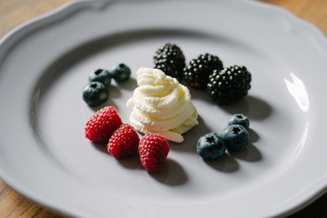 Close up view on a delicious, decorative dessert made from berry mix (raspberries, blueberries, raspberries) and whipped cream on a white plate.