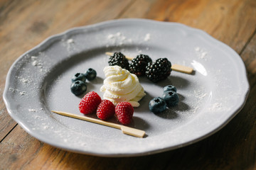 Close up view on a delicious, decorative dessert made from berry mix (raspberries, blueberries, raspberries) and whipped cream on a white plate.