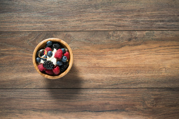Obraz na płótnie Canvas Delicious sweet dessert made from berry mix (raspberries, blueberries and blackberries) with whipped cream in a wooden bowl on a wooden background. Close up.