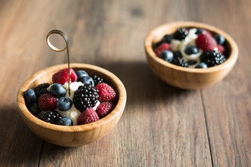 Delicious sweet dessert made from berry mix (raspberries, blueberries and blackberries) with whipped cream in a wooden bowl on a wooden background. Close up.