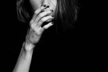 #metoo movement concept. Closeup portrait of young woman hiding face with hand, isolated on black background. Human emotion, expression, rights & communication. Text space. Monochrome studio shot