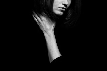 #metoo movement concept. Closeup portrait of young woman hiding face, posing with hand on neck, isolated on black background. Human emotion, expression, rights & communication. Text space. Monochrome