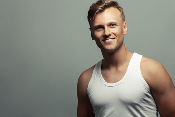 Male beauty, boy next door concept. Portrait of smiling 30-year-old man standing over gray background. Close up. Copy-space. Sportsman style. Wavy glossy blond hair. Studio shot