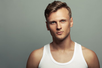 Male beauty, boy next door concept. Portrait of smiling 30-year-old man standing over gray background. Close up. Copy-space. Sportsman style. Wavy glossy blond hair. Studio shot