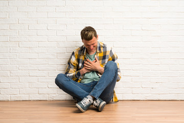 Obraz na płótnie Canvas Blonde man sitting on the floor having a pain in the heart