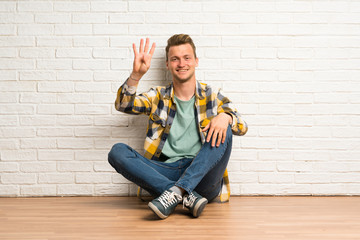 Blonde man sitting on the floor happy and counting four with fingers