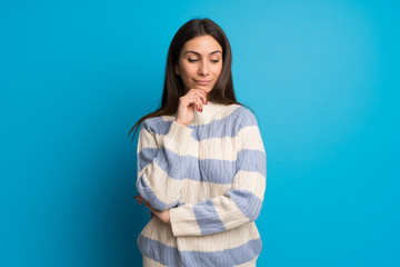 Young woman over blue wall looking down with the hand on the chin