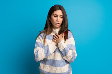 Young woman over blue wall having a pain in the heart