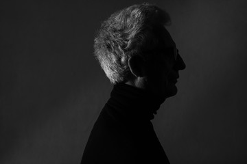 Movie poster, book cover, film noir concept. Arty profile portrait of fashionable mature man wearing trendy black turtleneck. Silver hair. German expressionism style. Contrastive monochrome shot