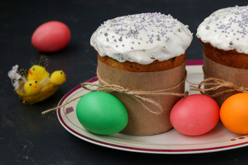 Easter cakes and colorful eggs are located on a plate against a dark background