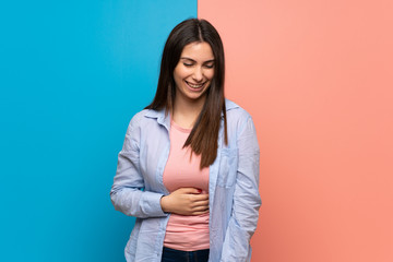 Young woman over pink and blue wall smiling a lot while putting hands on chest