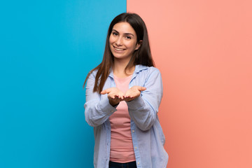 Young woman over pink and blue wall holding copyspace imaginary on the palm to insert an ad