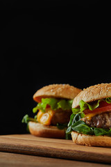 selective focus of delicious meat burgers with cheese and sesame isolated on black