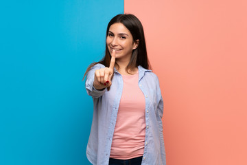 Young woman over pink and blue wall showing and lifting a finger