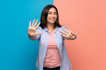 Young woman over pink and blue wall counting nine with fingers