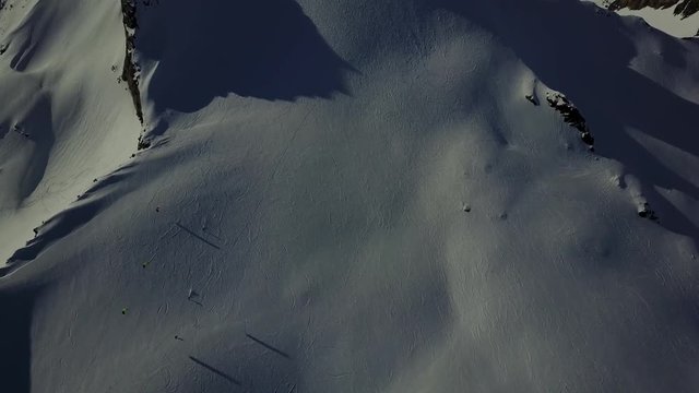 aerial view from far above,flying over a very large snow covered mountain.afternoon daylight with three little tiny snowkiters enjoying snowboarding on the scene.traveled to norway in 4K 30fps