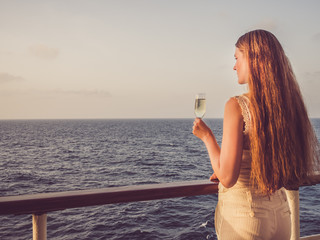 Cute woman holding a beautiful glass of champagne on the open deck of a cruise liner against the...