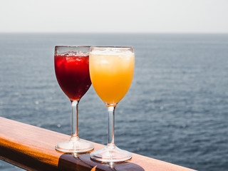 Beautiful wineglass with a cocktail and ice cubes, standing on the open deck against the backdrop of sea waves. Side view, close-up. Concept of leisure and travel