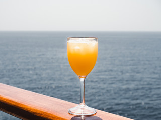 Beautiful wineglass with a cocktail and ice cubes, standing on the open deck against the backdrop...
