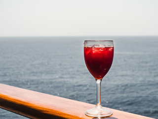 Beautiful wineglass with a cocktail and ice cubes, standing on the open deck against the backdrop of sea waves. Side view, close-up. Concept of leisure and travel