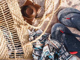 Wicker basket, vintage camera and shawl on sand background. Top view, close-up