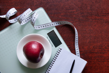 The concept of healthy nutrition, fitness and weight loss. Weights, measuring tape, apple, open notebook and pencil on the table. 