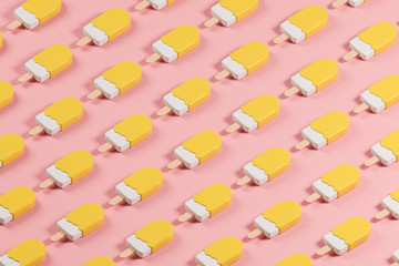 Isometric pattern made of yellow glossy lolly ice cream on the pink table.