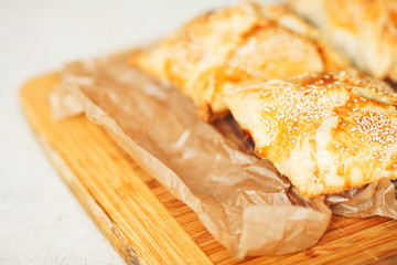 Vegetarian food concept. Baked chaussons with seeds of sesame on wooden board with parchment paper in cafe. French cuisine. Close up. Indoor shot