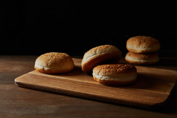 delicious buns with sesame on wooden chopping board isolated on black