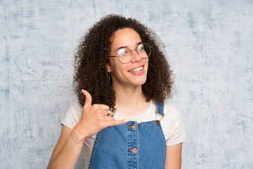 Dominican woman with overalls over grunge wall making phone gesture