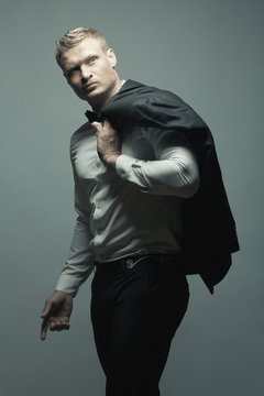 Male fashion, beauty concept. Portrait of brutal young man with short wet blond hair wearing black suit, posing over gray background. Classic style. Studio shot