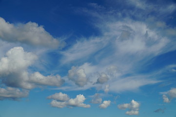 Clouds in the blue sky on a Sunny day. The wind disperses the dense clouds, alternating with thin, through which Shine through the sky.