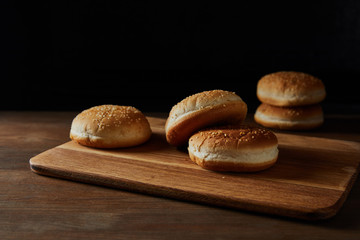 tasty buns with sesame on wooden chopping board isolated on black