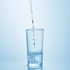 Pouring water into glass on white background. Water spilled on the table.