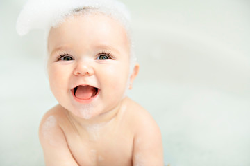 A Baby girl bathes in a bath with foam and soap bubbles - obrazy, fototapety, plakaty