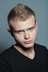 Fototapeta premium Close up portrait of young man with short blond hair and freckles on face wearing black t-shirt and posing over gray background. Hipster style. Studio shot