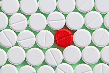 Top view of a pile of white medicine pills on a white surface. One tablet of red medication. Vaccine concept