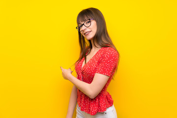 Young woman over yellow wall pointing back